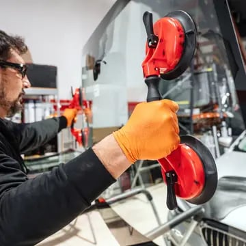 Automobile technician worker replacing windscreen or windshield of a car in auto service station garage